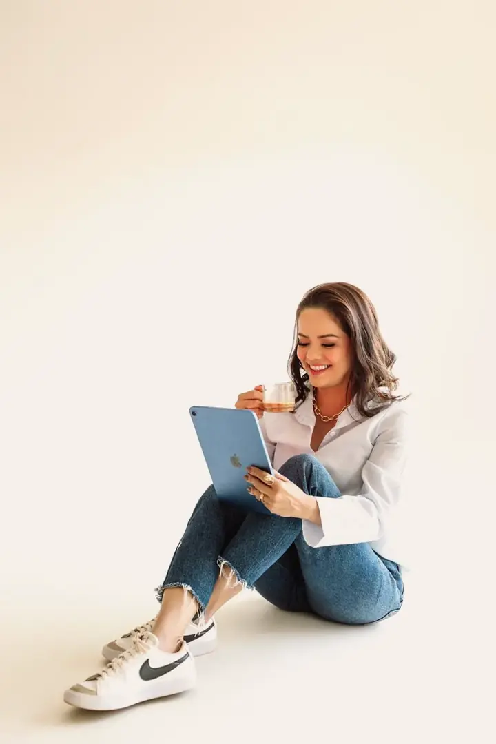 Cristia Melisa sentada no chão, sorrindo, com um tablet e uma xícara de chá