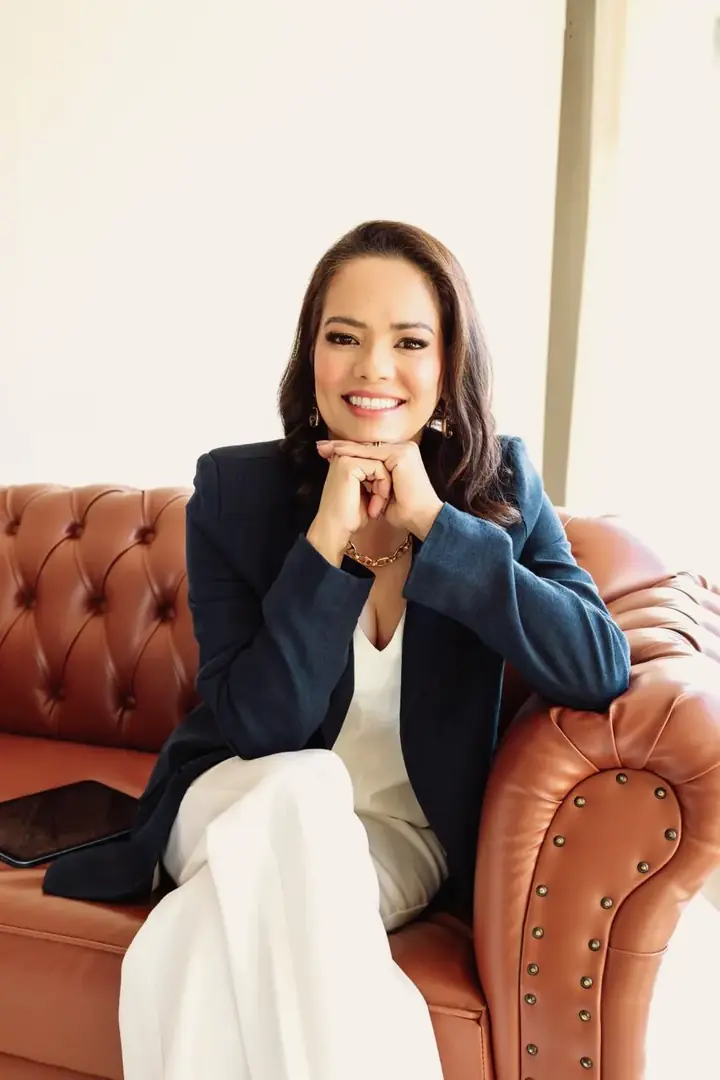 Cristia Melisa sorrindo, sentada em um sofá de couro com as mãos apoiadas sob o queixo